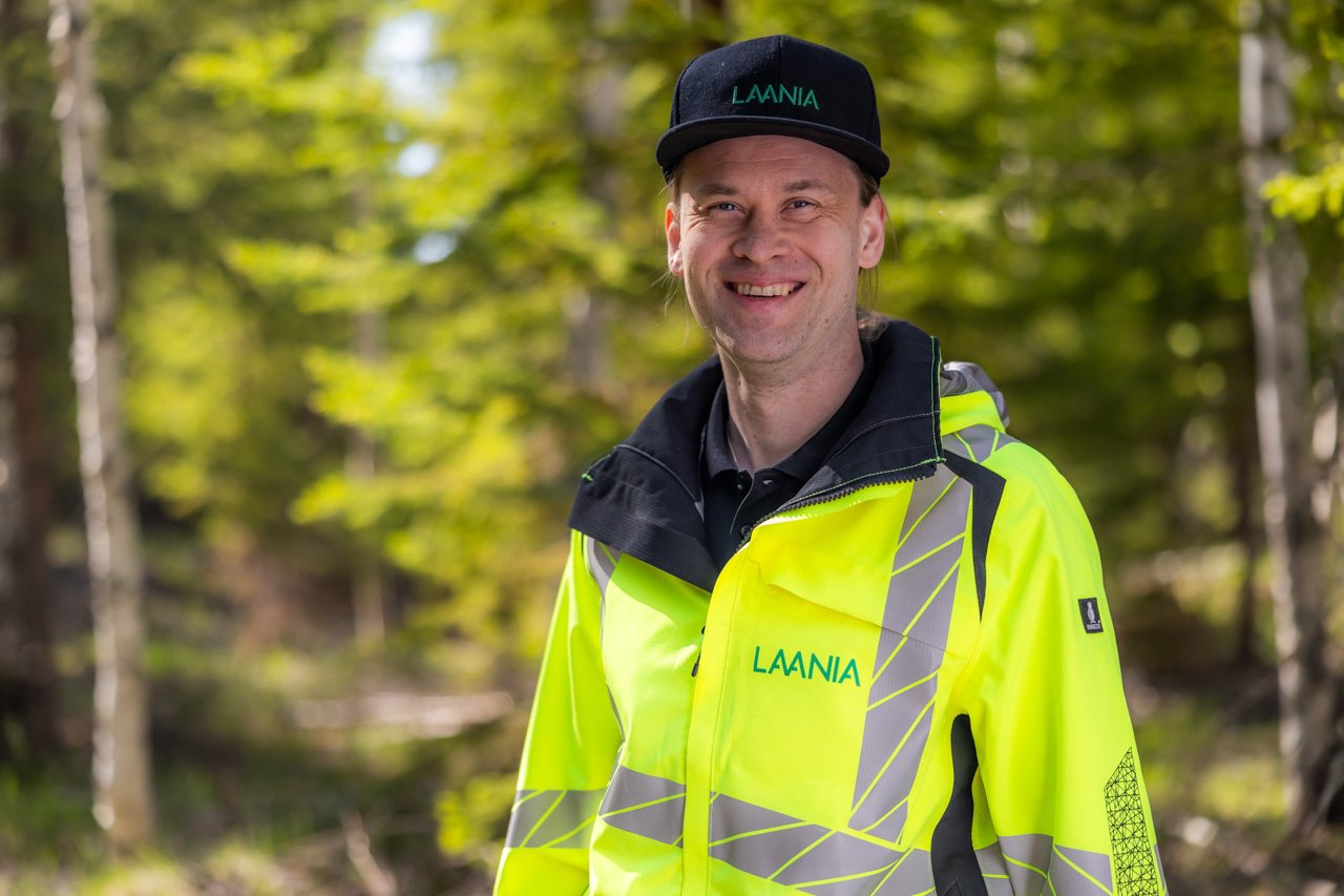 Laanian työntekijä hymyilee iloisena metsässä.