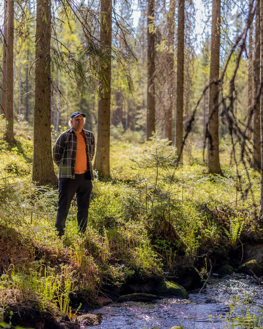 Metsänomistaja seisoo virtaavan puron reunalla ja katselee eteenpäin.