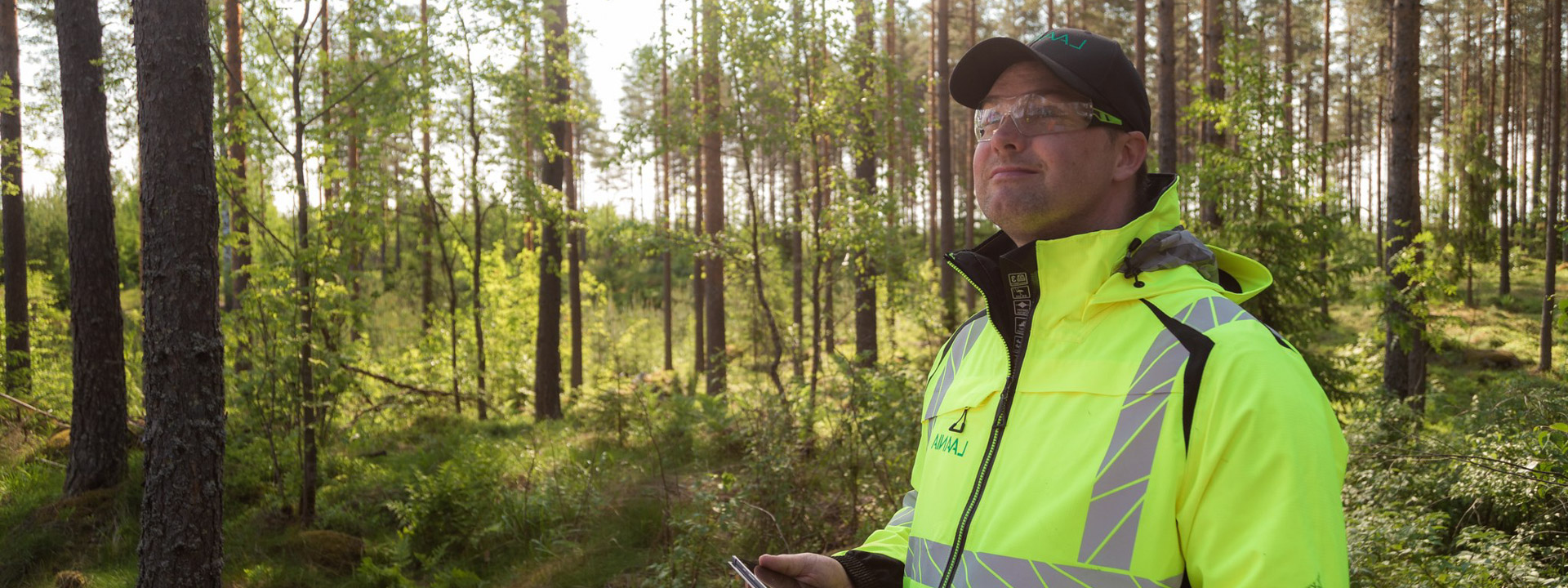 Metsäasiantuntija hymyilee metsässä.