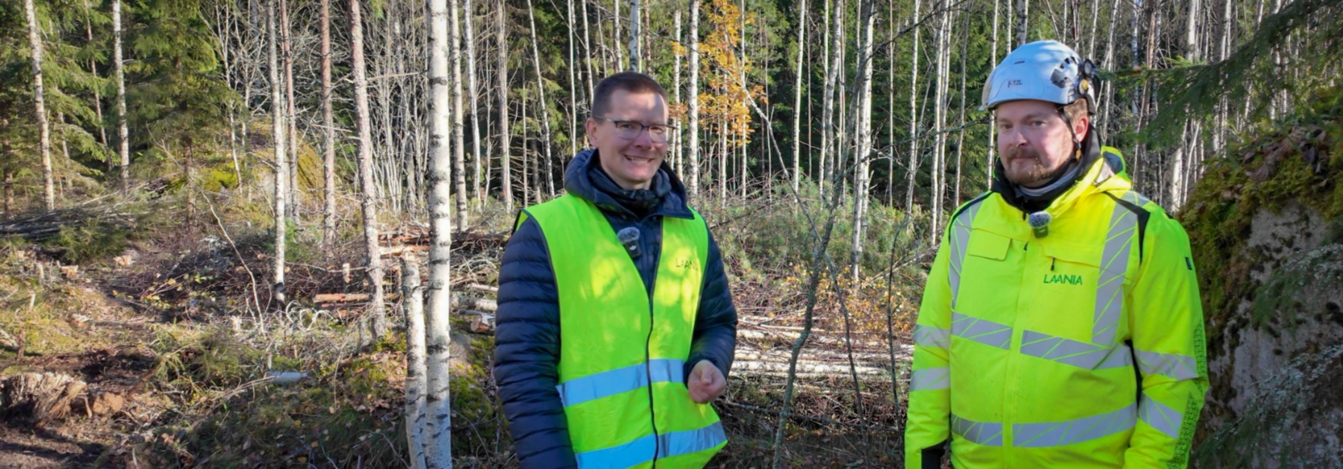 Miehet seisovat metsätyömaalla huomioliivit päällään.